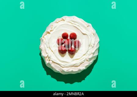 Torta Pavlova fatta in casa, sormontata da fragole fresche, minimalista su un tavolo verde. Deliziosa meringa piena di panna montata. Foto Stock