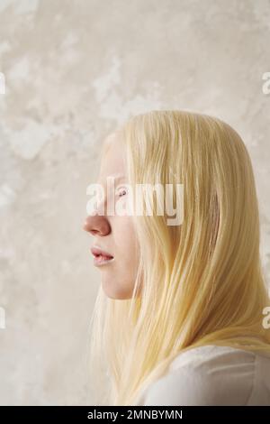 Giovane donna albina serena con capelli lisci lunghi guardando in avanti mentre si trova davanti alla fotocamera sopra la parete di colore pastello in isolamento Foto Stock