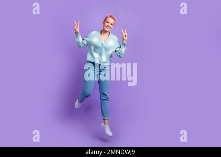 Full body length foto del giovane hipster spensierate lady jumping indossare nuova collezione vestito mostra v-segno blog isolato su sfondo di colore viola Foto Stock