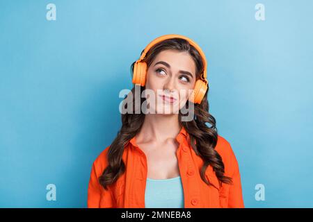 Foto di giovane donna attraente indossare cuffie guardare scettico spazio vuoto vestito elegante aspetto arancione isolato su sfondo di colore blu Foto Stock