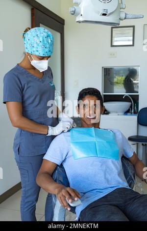 Dentista femminile in studio dentistico che parla con un giovane paziente maschio e si prepara al trattamento. Foto Stock