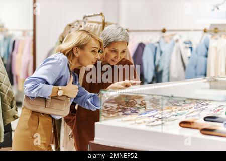 Vista laterale ritratto di donna adulta sorridente con madre shopping insieme in boutique di abbigliamento e guardare gli accessori Foto Stock
