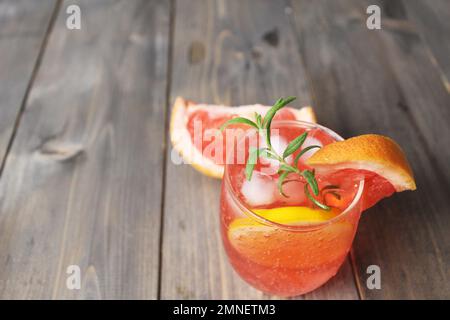 bevi il succo di limonata di pompelmo d'arancia rossa in un bicchiere con una slitta e un rosmarino di menta su uno sfondo grigio con un posto per il testo. Rinfrescare i freddi Foto Stock