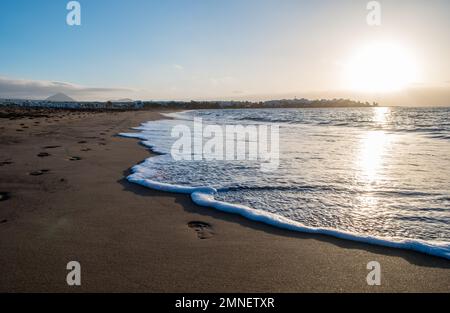 Spiaggia di Lanzarote al mattino con le orme e un'onda carezzando la sabbia dorata. Alba sulla spiaggia senza persone. Foto Stock