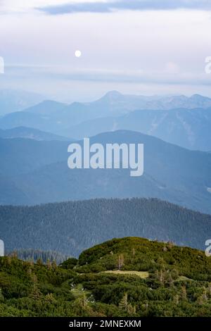 Vista dalla cima di Benediktenwand al tramonto con la luna, preAlpi Bavaresi, Baviera, Germania Foto Stock