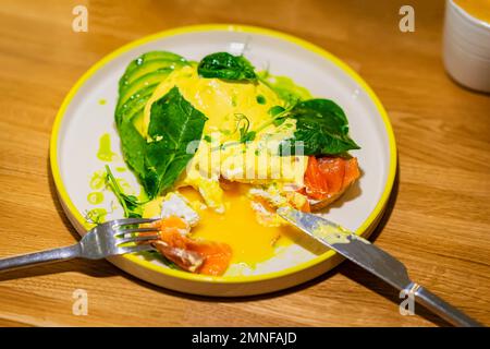 Colazione al mattino. Sandwich all'uovo in camicia con avocado, salmone e caffè su tavolo di legno Foto Stock