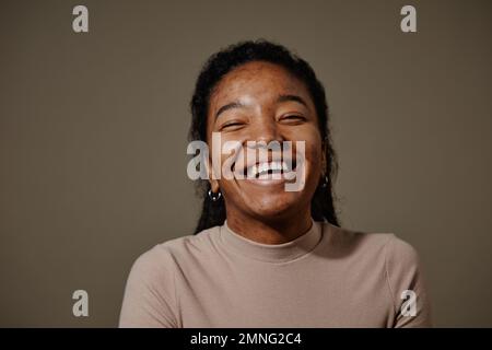 Ritratto candido di giovane donna nera che ride contro sfondo beige neutro in studio focus sulla struttura della pelle Foto Stock