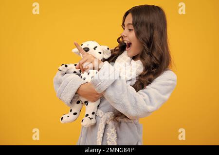 Bambino ragazza teen in abbigliamento casual tenendo peluche giocattolo isolato su sfondo giallo, infanzia felice. Ragazza teen stupita. Bambino in pigiama, Buongiorno Foto Stock