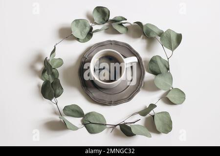 Corona rotonda fatta di foglie di eucalipto verde secco e rami isolati su sfondo bianco tavolo. Composizione floreale decorativa. Tazza di caffè Foto Stock