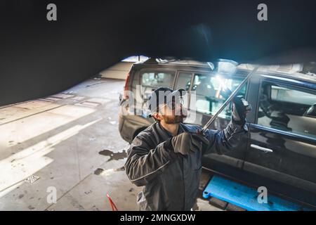 Un meccanico esperto con una luce a LED ispeziona un'auto su un ascensore in una stazione di riparazione. Foto di alta qualità Foto Stock