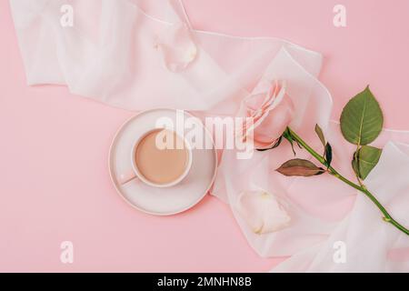 Una tazza da caffè e rosa rosa su tessuto di seta bianca. Concetto di vacanza. Vista dall'alto, disposizione piatta Foto Stock