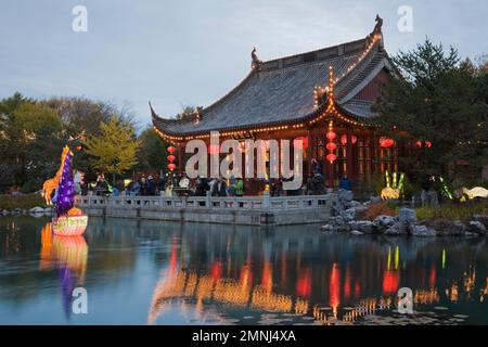 Padiglione della Friendship Hall e lanterne di giraffa e giunca cinese illuminate sul Dream Lake durante l'annuale mostra Magic of Lanterns nel Giardino Cinese. Foto Stock