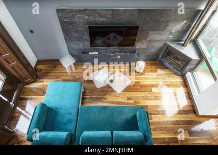 Soggiorno di una casa con camino in un angolo con tubo metallico, grande tv sulla parete di fronte a un divano con chaise longue verde velluto Foto Stock