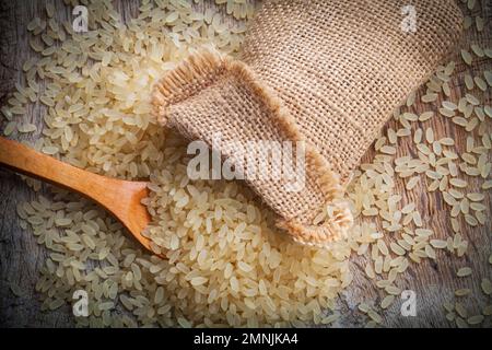 giallo riso marrone, usato per risotto in juta di sacco di burlap su un tagliere di legno Foto Stock