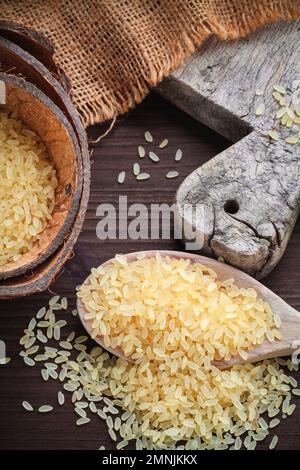 giallo riso marrone, usato per risotto in juta di sacco di burlap su un tagliere di legno Foto Stock