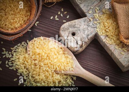 giallo riso marrone, usato per risotto in juta di sacco di burlap su un tagliere di legno Foto Stock