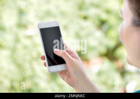 Donna che tiene in mano uno smartphone all'aperto con uno sfondo verde naturale Foto Stock