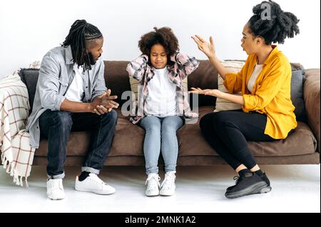 Difficoltà nel rapporto dei genitori con il bambino, conflitto. I genitori afroamericani ordinano le cose fuori con la loro figlia del prescolare, grida a lei, il bambino ha coperto le sue orecchie, ignora. Abuso Foto Stock