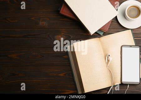 Libri, caffè, auricolari e telefono cellulare su tavolo di legno, piatto. Spazio per il testo Foto Stock