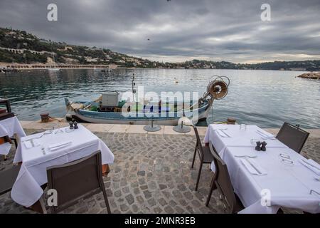 Un pescatore è ormeggiato di fronte alla terrazza del ristorante a cui consegna il pesce fresco la società Spada, su richiesta dello Stato francese, installa una chiatta di recupero relitto nella baia di Villefranche-sur-Mer per preparare la stagione estiva ed evitare l'inquinamento marino. Foto Stock