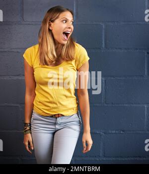 Che... una giovane donna che guarda stupito contro uno sfondo muro di mattoni. Foto Stock