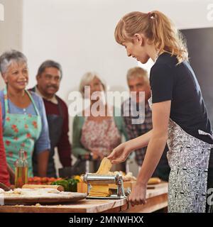 Mostrare loro come tagliare la bolletta della spesa. una donna che mostra alla sua classe come preparare la pasta. Foto Stock