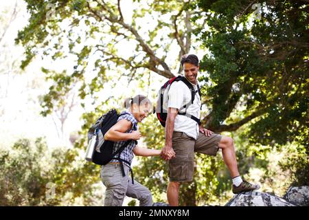 In prima linea. Escursionista maschio che tiene la sua mano girlfriends mentre si arrampicano su una roccia - copyspace. Foto Stock