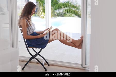 Prendetevi un po' di tempo per voi stessi. una giovane donna che legge un libro a casa. Foto Stock