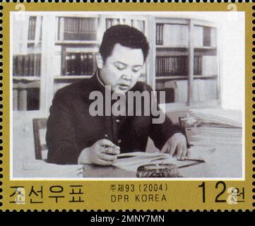 Francobollo nordcoreano del 2004 con Kim Jong il ad una scrivania con scaffali, taglio da 12 won, DPR Korea. Foto Stock