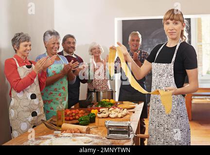 E questo è come si fa la pasta. Ritratto di una donna che tiene la pasta appena fatta con i suoi studenti sullo sfondo. Foto Stock