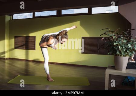 Giovane donna atletica pratica yoga, facendo una variazione di Adhomukha Uthitahasta Padangushthasana esercizio numero 2, equilibrando su una gamba, esercizio Foto Stock
