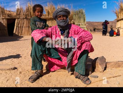 L'uomo Tuareg con il suo bambino siede davanti alla sua casa di canna, Nord Africa, Tamanrasset, Algeria Foto Stock