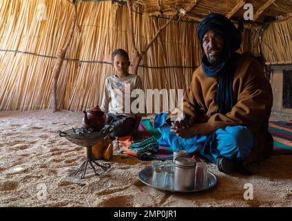 Tuareg uomo e figlio all'interno di una casa di ravizzone che prepara il tè, Nord Africa, Tamanrasset, Algeria Foto Stock