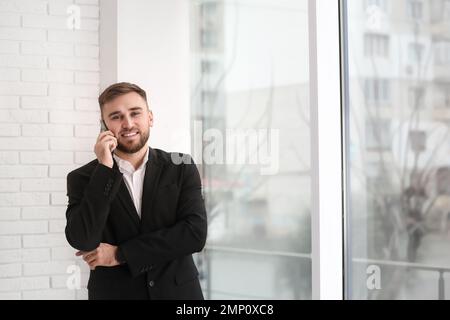 Giovane uomo d'affari che parla al telefono vicino alla finestra di casa Foto Stock