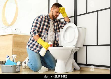 Giovane uomo che sente disgusto mentre pulisce il water ciotola in bagno Foto Stock