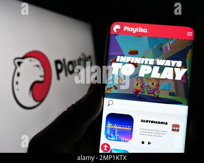 Persona che tiene il cellulare con la pagina web della società israeliana di giochi mobili Playtika Ltd. Sullo schermo di fronte al logo. Messa a fuoco al centro del display del telefono. Foto Stock