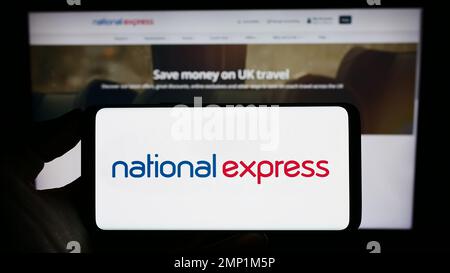 Persona che tiene il cellulare con il logo della società britannica National Express Group plc (NX) sullo schermo di fronte alla pagina web. Messa a fuoco sul display del telefono. Foto Stock