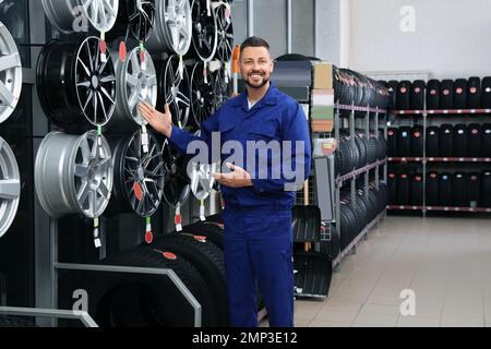 Meccanico maschile vicino a pneumatici auto e cerchi in lega in negozio auto Foto Stock