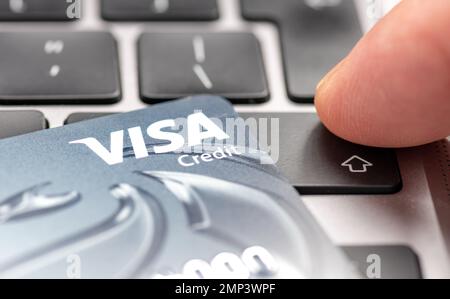 Londra. UK- 01.29.2023. Una carta di credito Visa sulla parte superiore di un computer portatile con una persona che preme il tasto invio. Foto Stock