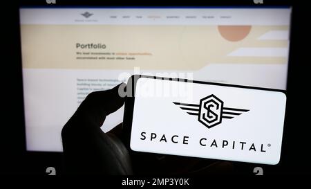 Persona che tiene il cellulare con il logo della società americana di capitale di rischio Space Capital LP sullo schermo di fronte al sito web. Messa a fuoco sul display del telefono. Foto Stock