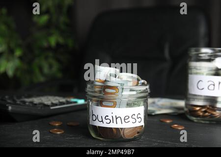 Vaso di vetro con soldi e tag BUSINESS sul tavolo nero Foto Stock