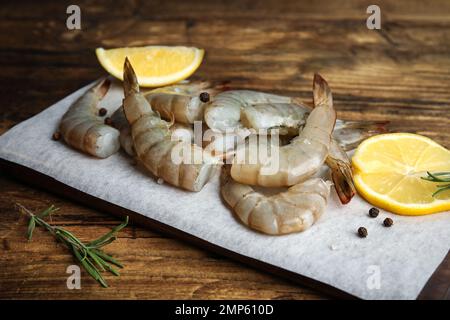 Gamberetti freschi crudi con limone e rosmarino su tavola di legno, primo piano Foto Stock