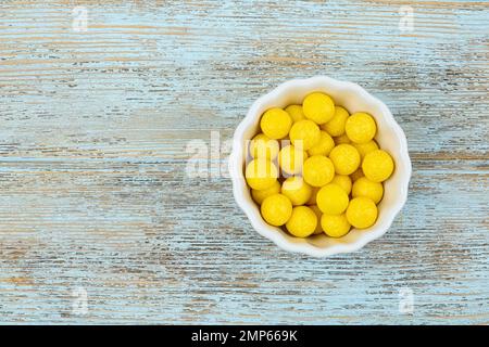 Deliziose gomme da masticare al limone in ciotola su sfondo di legno azzurro, vista dall'alto. Spazio per il testo Foto Stock