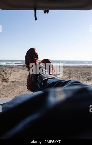 Gambe dell'uomo in jeans blu e scarpe da trekking giacenti all'interno di un furgone sulla spiaggia. Foto Stock