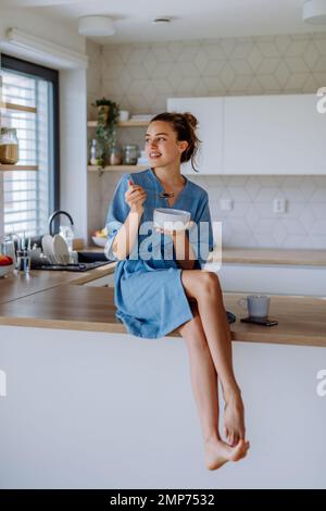 Giovane donna che ha muesli per la colazione in cucina, la routine mattutina e concetto di stile di vita sano. Foto Stock