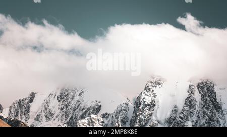 Le cime di montagne di pietra con lingue di ghiacciai e neve sono coperte di nuvole bianche e nebbia in Altai. Foto Stock