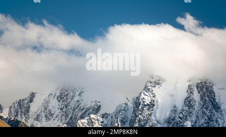 Panorama delle cime delle montagne di pietra con lingue di ghiacciai e neve ricoperta di nuvole bianche e nebbia in Altai. Foto Stock