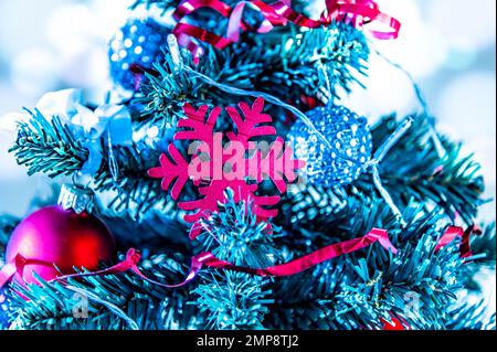 Primo piano di un piccolo albero di Natale decorato con palle rosse, catene e un fiocco di neve rosso. Colori freddi in inverno Foto Stock