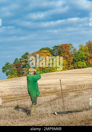 Un uomo con un fucile all'inizio di un fagiano spara in un caldo autunno pomeriggio di sole Foto Stock