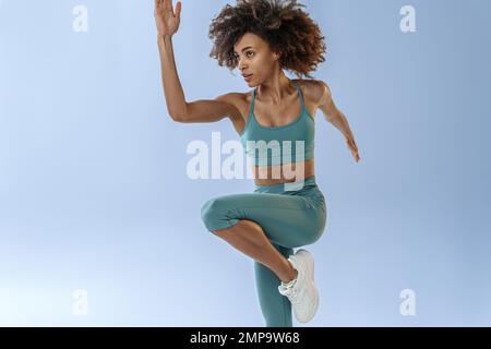 Primo piano della donna sportiva che corre in Mid-Air esercizio durante l'allenamento cardio su sfondo studio Foto Stock